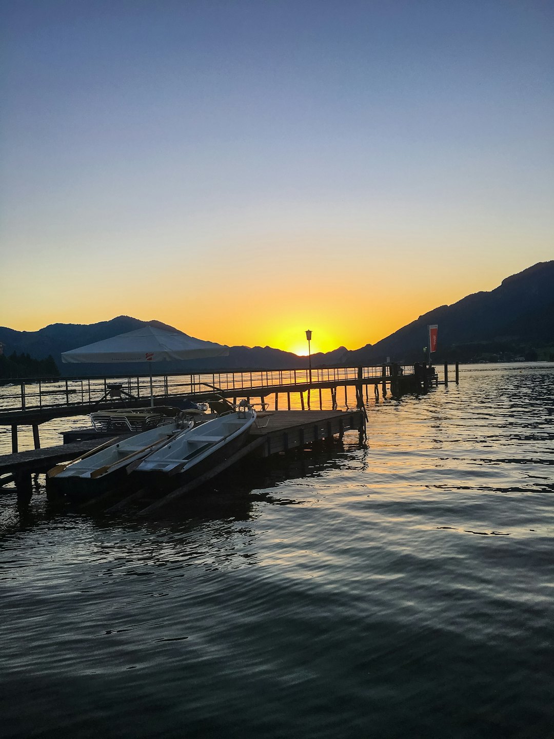 Hölzerne Seebrücke mit Ruderbooten bei Sonnenuntergang auf einem See.