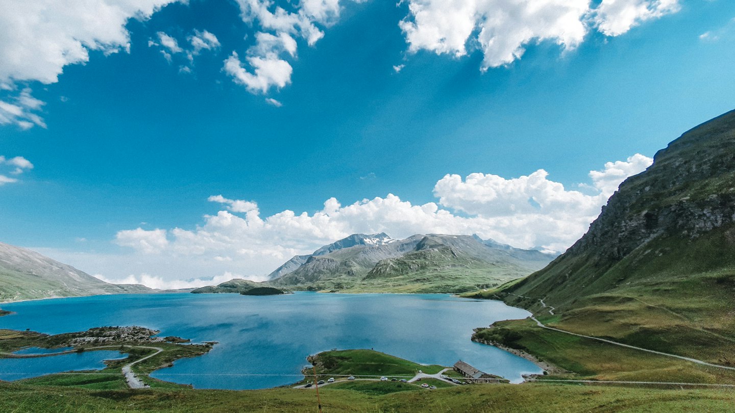 Schneebedeckte Berggipfel überblicken einen ruhigen blauen See in der Nähe von grünen Hügeln.